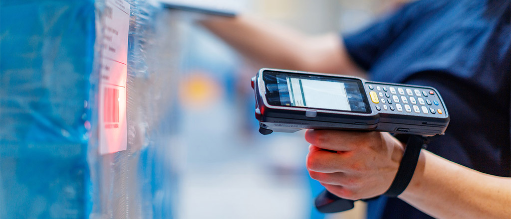 Woman in warehouse aiming at product, holding barcode reader